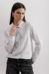 Camisa blanca a rayas verticales negras, de corte clásico, con cuello camisero y mangas largas con puños abotonados.