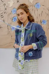 Chaqueta azul de pana con bordados florales a mano y a máquina, cuello camisero con detalle de puntilla y bolsillos frontales.