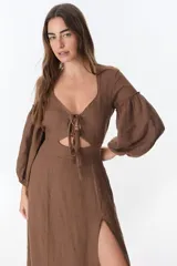 Vestido color beige de lino, con escote en V, mangas largas abullonadas y lazos frontales. Tiene corte a la cintura y falda larga con tajo frontal.