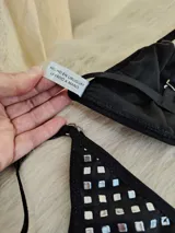 Conjunto de bikini negro con tachas plateadas. El corpiño es de corte triangular con breteles regulables y aro metálico central. La bombacha es tipo colaless con tiras laterales regulables.