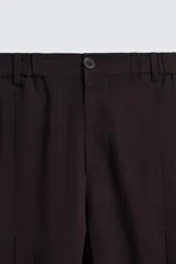 Pantalón marrón oscuro de corte ancho, confeccionado en mezcla de algodón y lino. Presenta cintura elástica, bolsillos laterales y traseros, pliegues frontales y cierre con cremallera y botón.