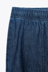 Pantalón de jean azul con cintura elástica ajustable con cordones, tiro medio y bolsillos de parche en la parte trasera.