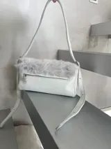 Cartera mini de cuero blanco con solapa de pelo gris y herrajes metálicos plateados.