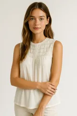 Blusa color crema de algodón con cuello a la base y detalle de broderie en el frente. Sin mangas y con botón en la parte posterior del cuello.