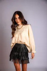 Camisa color crema con cuello alto y mangas largas con volados en los puños. Presenta detalles de crochet y broderie en el frente.