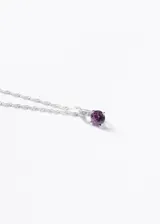Collar con cadena de plata 925 de eslabones tipo torsada, con un dije colgante que presenta una piedra central de zirconia facetada de color violeta, engastada en una montura con detalles de piedras pequeñas a lo largo del soporte.