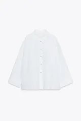 Camisa blanca oversize de popelina de algodón, con cuello solapa, manga larga con puños y cierre frontal con botones ocultos. Detalle de hilo de contraste en los botones.