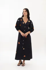 Vestido midi color arena con escote en V, mangas 3/4 abullonadas y cierre frontal con botones. Presenta bordados de motivos marinos.