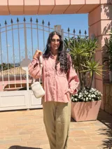 Bandolera pequeña tipo 'phone bag' de símil cuero color rosado pálido, con cierre de cremallera y correa ancha de tela con diseño de chevron en tonos claros.