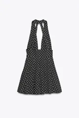 Vestido corto negro con lunares blancos, cuello halter y escote pico. Detalle de lazo en la espalda y cierre lateral con cremallera oculta.