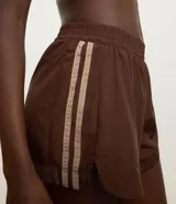 Short deportivo femenino modelo runner, color marrón chocolate con cintura elástica y rayas laterales color crema.