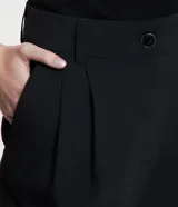 Pantalón negro de corte carrot, con pliegues delanteros, abotonado frontal y detalle en el bajo.