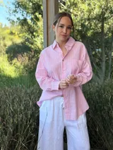 Camisa holgada a rayas verticales color beige y blanco, con cuello clásico, manga larga, bolsillo en el pecho y cierre frontal con botones nacarados.