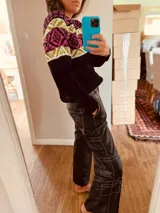 Sweater negro con diseño geométrico en blanco, rosa y amarillo en la parte superior.