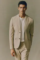 Blazer color beige de corte slim fit, con solapas de muesca finas, botonadura sencilla con cierre de dos botones, bolsillo superior, bolsillos delanteros con solapa, tres bolsillos interiores, botones decorativos en los puños y abertura atrás.
