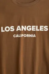 Remera color marrón con estampado blanco con la frase 'Los Ángeles California'. Corte recto y holgado, mangas cortas y cuello redondo.
