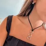 Collar con tres aros plateados en cadena de cuerda negra, diseño minimalista.