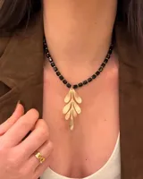 Collar corto con cuentas facetadas negras y detalles dorados, con dije colgante dorado en forma de hoja estilizada.