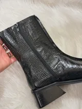 Bota negra de caña media con textura de cocodrilo, punta cuadrada y tacón bajo.