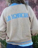 Saco de punto beige con cuello, puños y ruedo en azul. Estampado con letras azules en la espalda con el texto "LA IGNACIA".
