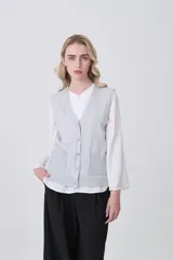 Chaleco de punto color crema, con cuello en V, cierre frontal de botones y dos bolsillos frontales.