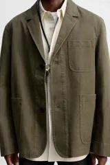 Blazer color verde oliva de algodón con efecto lavado, corte relaxed fit, cuello con solapas de muesca, manga larga y bolsillos frontales de plastrón. Cierre frontal con dos botones.