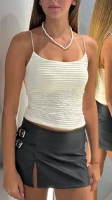 Minifalda de cuero sintético color negro, de tiro bajo, con tajo lateral y detalle de dos hebillas metálicas en el costado.