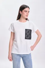 Remera blanca de algodón de corte recto, con cuello redondo y mangas cortas. Presenta un bolsillo de encaje negro en el pecho.