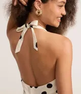 Vestido corto blanco con estampado de lunares negros, escote en V y espalda descubierta con tiras ajustables en el cuello.