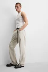 Pantalón de jean color beige, corte recto y relajado, con cintura ajustable con cordón interior, cinco bolsillos, efecto lavado y cierre frontal con cremallera y botón.