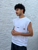 Musculosa blanca de corte amplio, con hombros caídos y cuello redondo. Presenta un estampado minimalista en negro en el pecho con la palabra "OSTEN" y un símbolo abstracto.