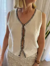 Chaleco tejido color arena con terminaciones en punto festón negro.