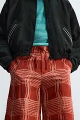 Short de baño color ladrillo con estampado de líneas curvas en color salmón. Tiene cintura elástica ajustable con cordón, bolsillos laterales y trasero.