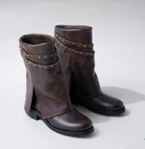 Bota corta de cuero color marrón con suela de goma negra, taco de madera de 3cm y caña de 25cm. Presenta una correa con hebilla y tachas pequeñas alrededor del tobillo.