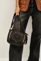 Cartera de cuero negro con diseño de flor mandala en relieve y apliques de tachas doradas y plateadas. Presenta flecos colgantes en uno de los laterales y correa ajustable para llevar al hombro o cruzada.