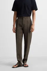 Pantalón de vestir color marrón oscuro, confeccionado en lino italiano. Presenta corte regular fit, cintura con pliegues, bolsillos laterales y traseros ribeteados, y terminación con dobladillo. Cierre frontal con cremallera y botón.