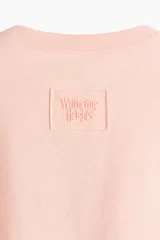 Camiseta de punto suave de algodón color rosado pálido, con corte holgado y mangas cortas. Presenta un motivo con texto en relieve/bordado en el frente que dice "Drive me mad".