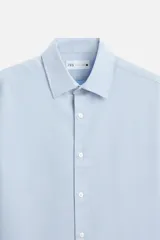 Camisa blanca de corte regular, cuello italiano, manga larga con puños abotonados y cierre frontal con botones.