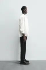 Pantalón chino negro de corte relajado (relaxed fit) con tiro medio, confeccionado en algodón con elasticidad. Presenta bolsillos delanteros y bolsillos traseros de vivo, con cierre frontal de cremallera y botón.