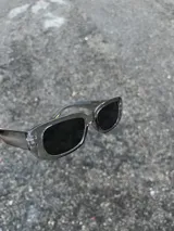 Gafas de sol rectangulares con montura transparente gris y lentes negras.