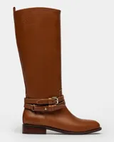 Bota de caña alta color marrón en cuero liso, con detalle de hebillas y tacón bajo.