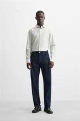 Camisa celeste a rayas verticales blancas, de corte recto, con cuello italiano abierto, mangas largas con puños abotonados y cierre frontal con botones.