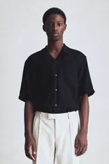 Camisa negra de manga corta en tejido arrugado. Modelo con cuello abierto, tapeta lisa, bolsillo superior y bajo recto. Corte estándar.