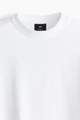 Remera blanca de algodón de peso medio, con cuello redondo ribeteado, hombros caídos y bajo recto. Corte oversized.