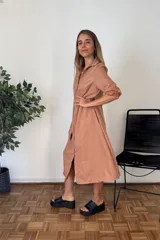 Vestido camisero largo color terracota/bronce, de manga larga con puños remangados, cuello solapa y cierre frontal de botones. Tiene un corte amplio y bolsillos laterales.