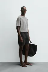 Bermuda negra regular fit confeccionada en tejido con mezcla de algodón y lino. Cintura elástica ajustable con cordón. Pliegues frontales. Bolsillos laterales y traseros de vivo. Cierre frontal con cremallera y botón.