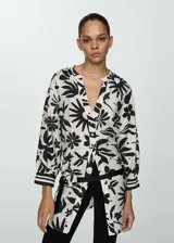 Blusa blanca con estampado floral negro, de tejido fluido, cuello de tira y cierre de lazo.
