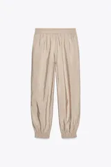 Pantalón de tiro medio color beige, con cintura elástica ajustable con cordones, bolsillos delanteros y puños elásticos en los tobillos.
