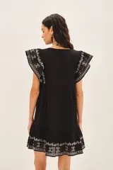 Vestido negro corto de corte amplio con bordados florales blancos en el frente, mangas y ruedo.