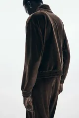 Campera corta de velour marrón oscuro, con cuello elevado, cierre frontal y bolsillos insertados al bies. Presenta elástico fruncido en puños y bajo.